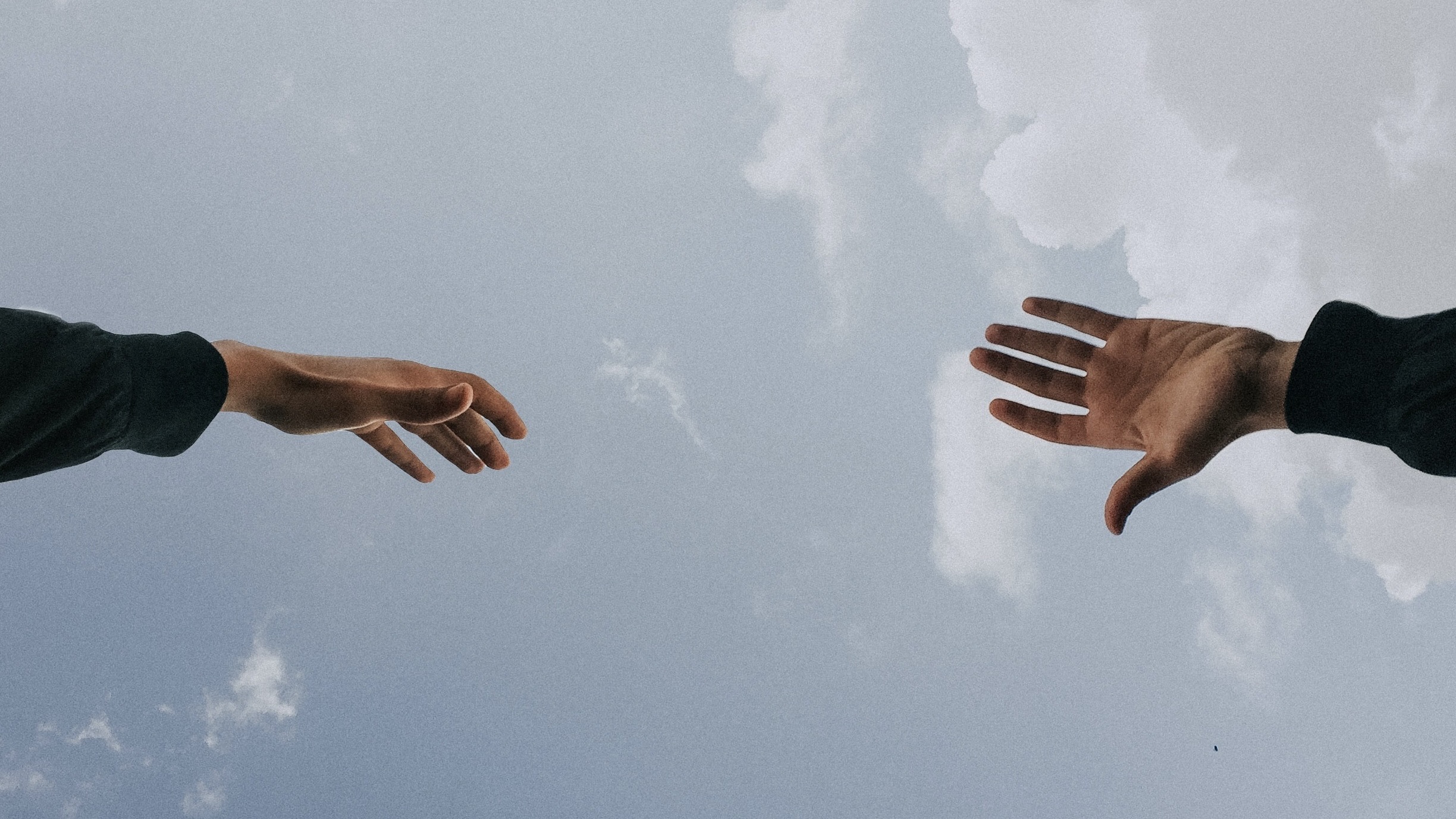 Image of two hands reaching for each other with sky in the background